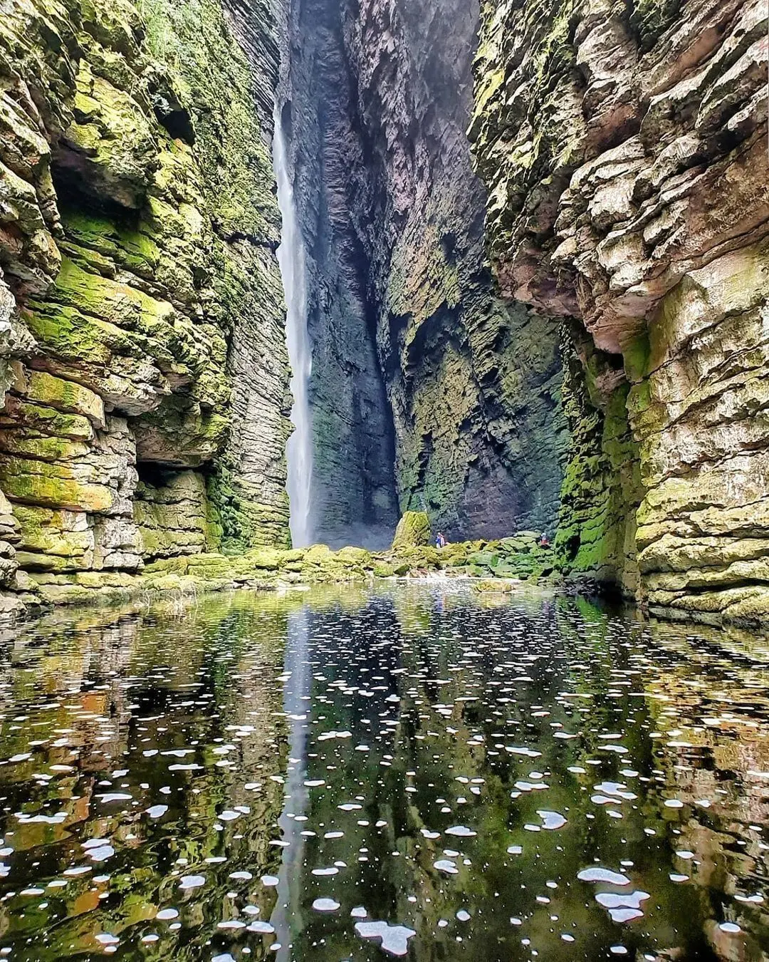 Cascada de la Fumacinha: caída de agua alta entre paredes cubiertas de musgo, reflejada en el pozo del cañón
