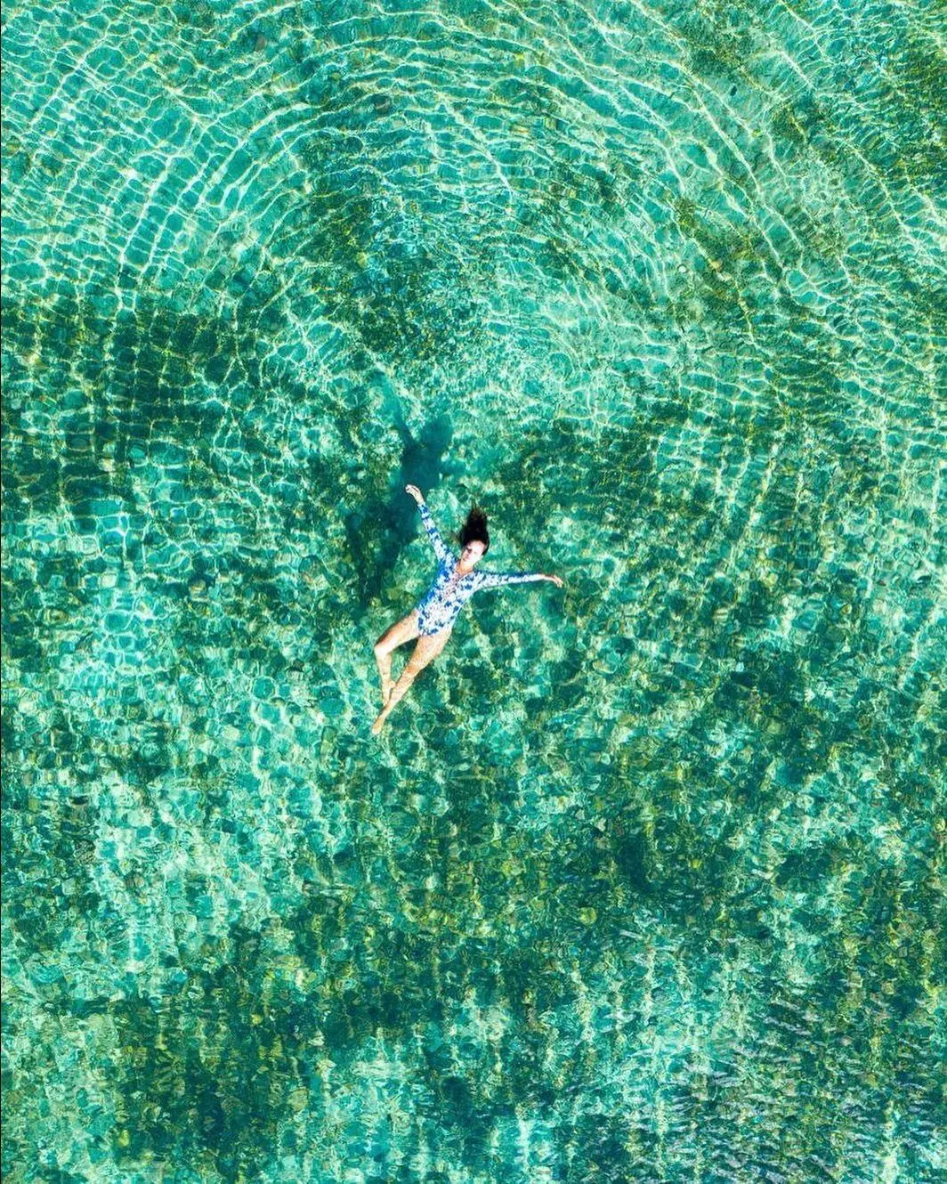 Top-down view of a woman floating in shallow, clear turquoise water