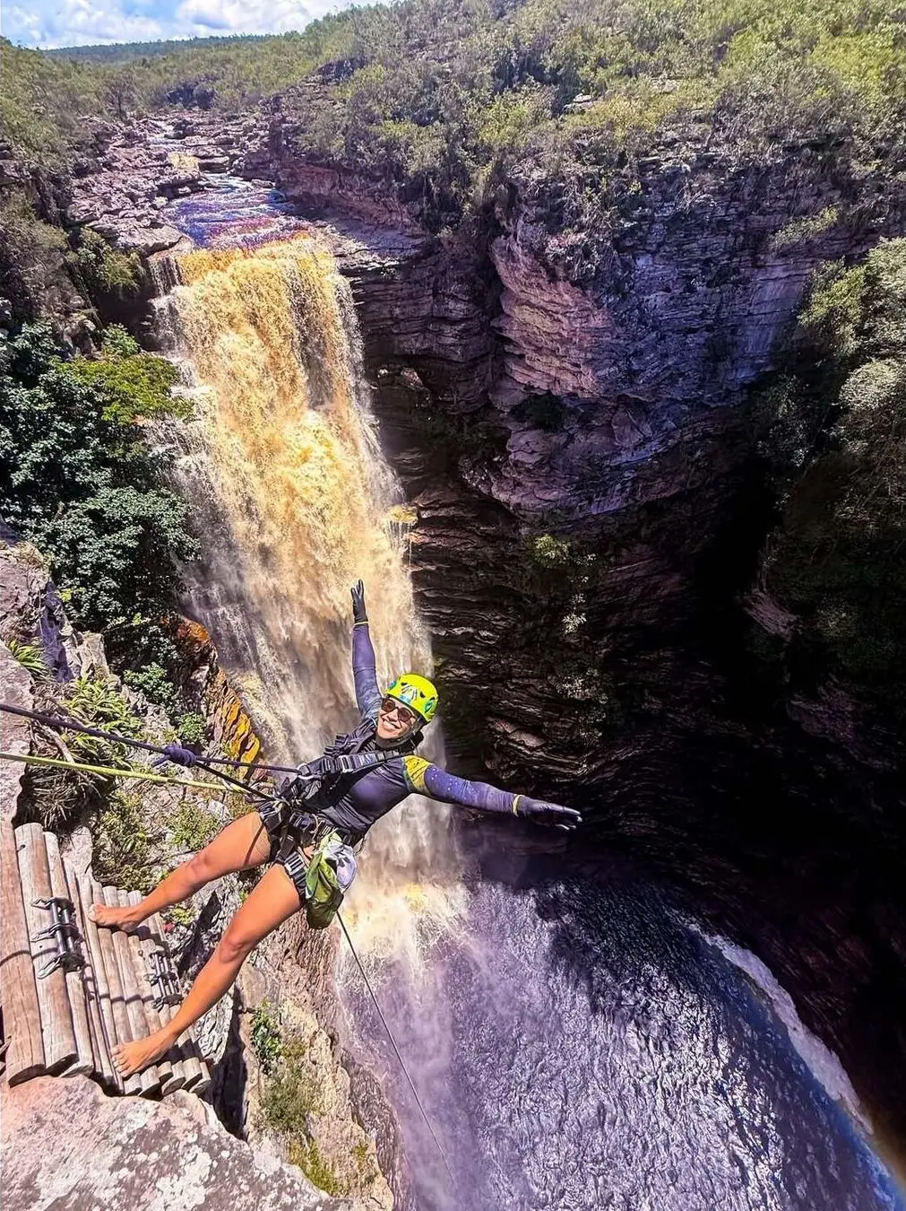 Woman in a helmet rappelling with open arms beside the Poço do Diabo waterfall