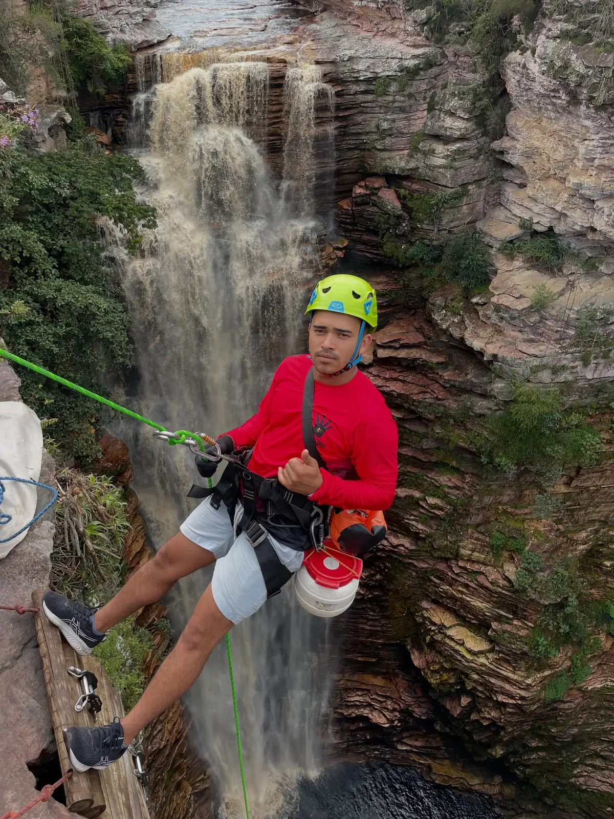 Young man in a green helmet rappelling beside the Poço do Diabo waterfall