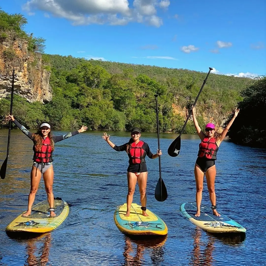 Three women in life vests paddling stand up paddleboards on a calm river between cliffs