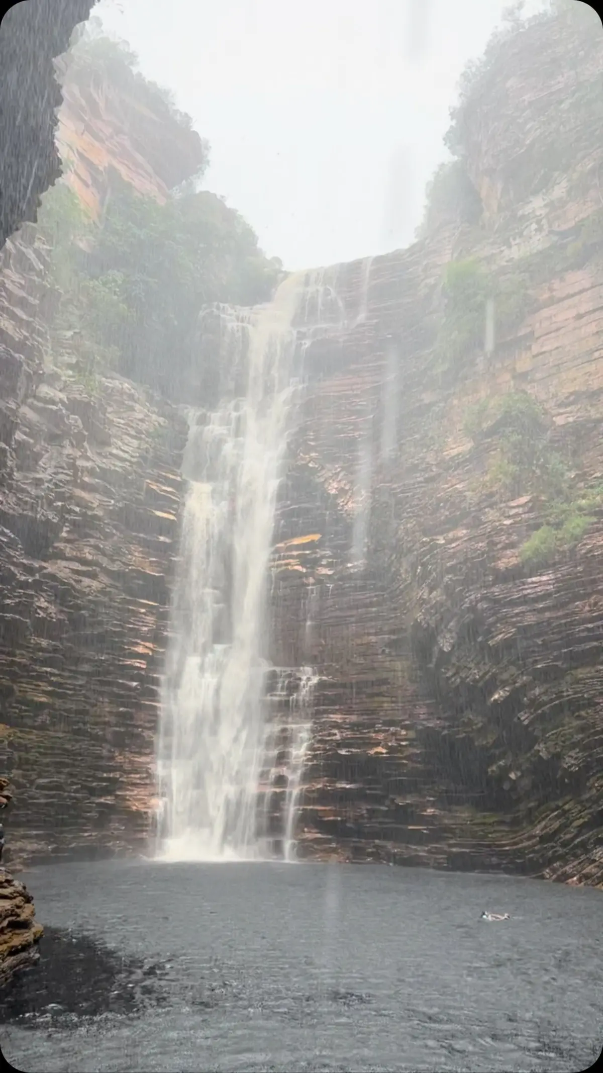 Buracão Waterfall seen from inside the narrow canyon, with dark, foamy water