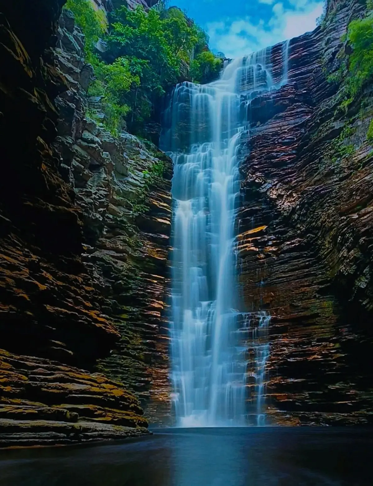 Buracão Waterfall falling between layered rock walls into a dark pool
