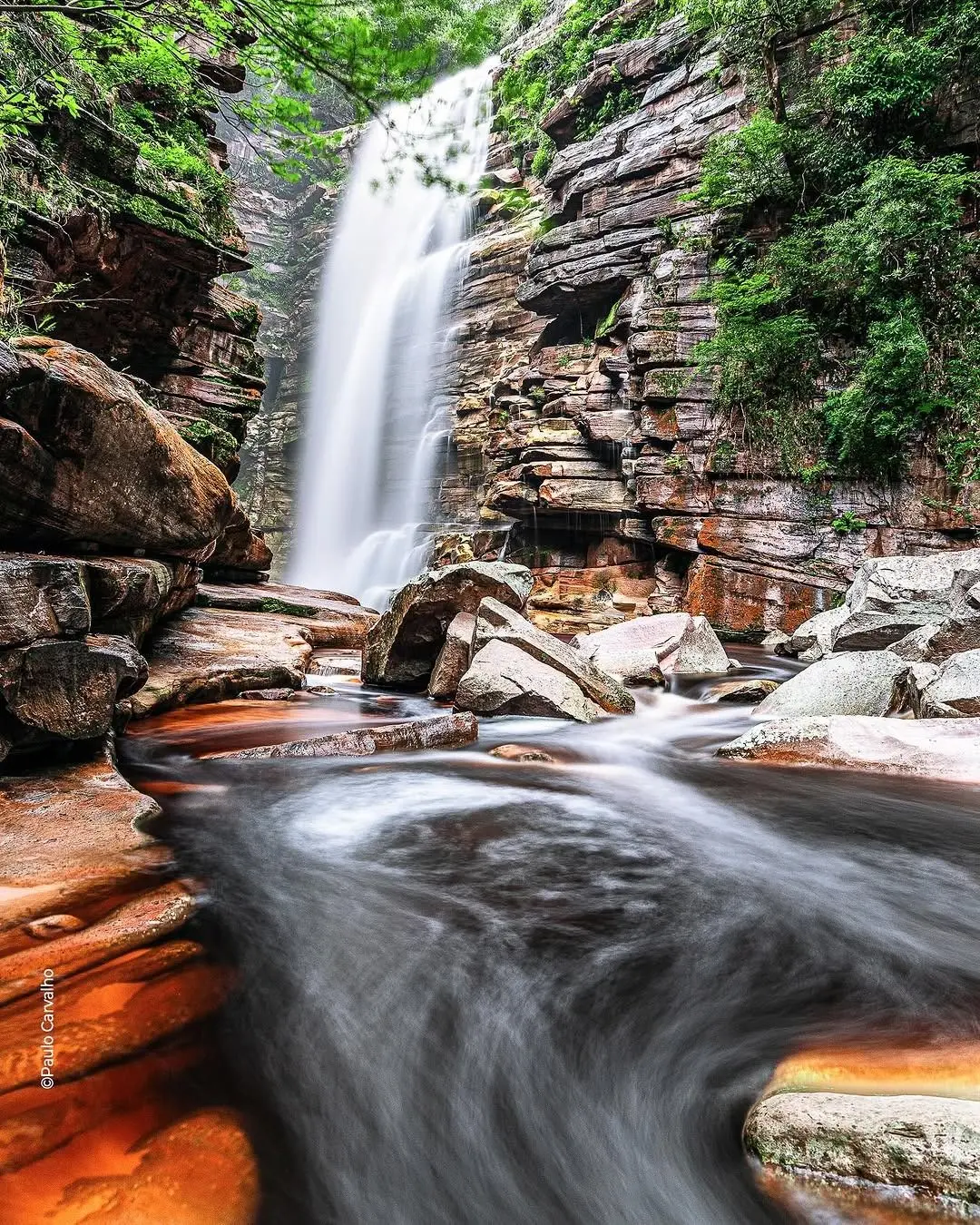 Mosquito Waterfall falling between layered rock walls, with the water running over orange stones