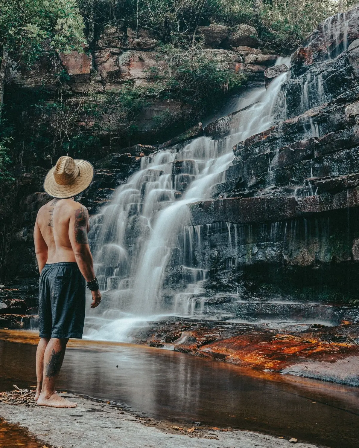 Man in a straw hat in front of a waterfall stepping down dark rock