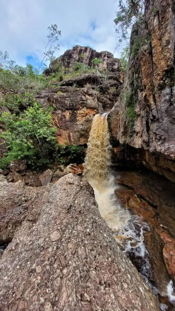 Tea-colored waterfall flowing between rock walls, next to a stone slab