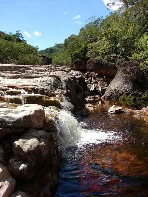 Small waterfall between stone slabs on a dark-water river surrounded by forest