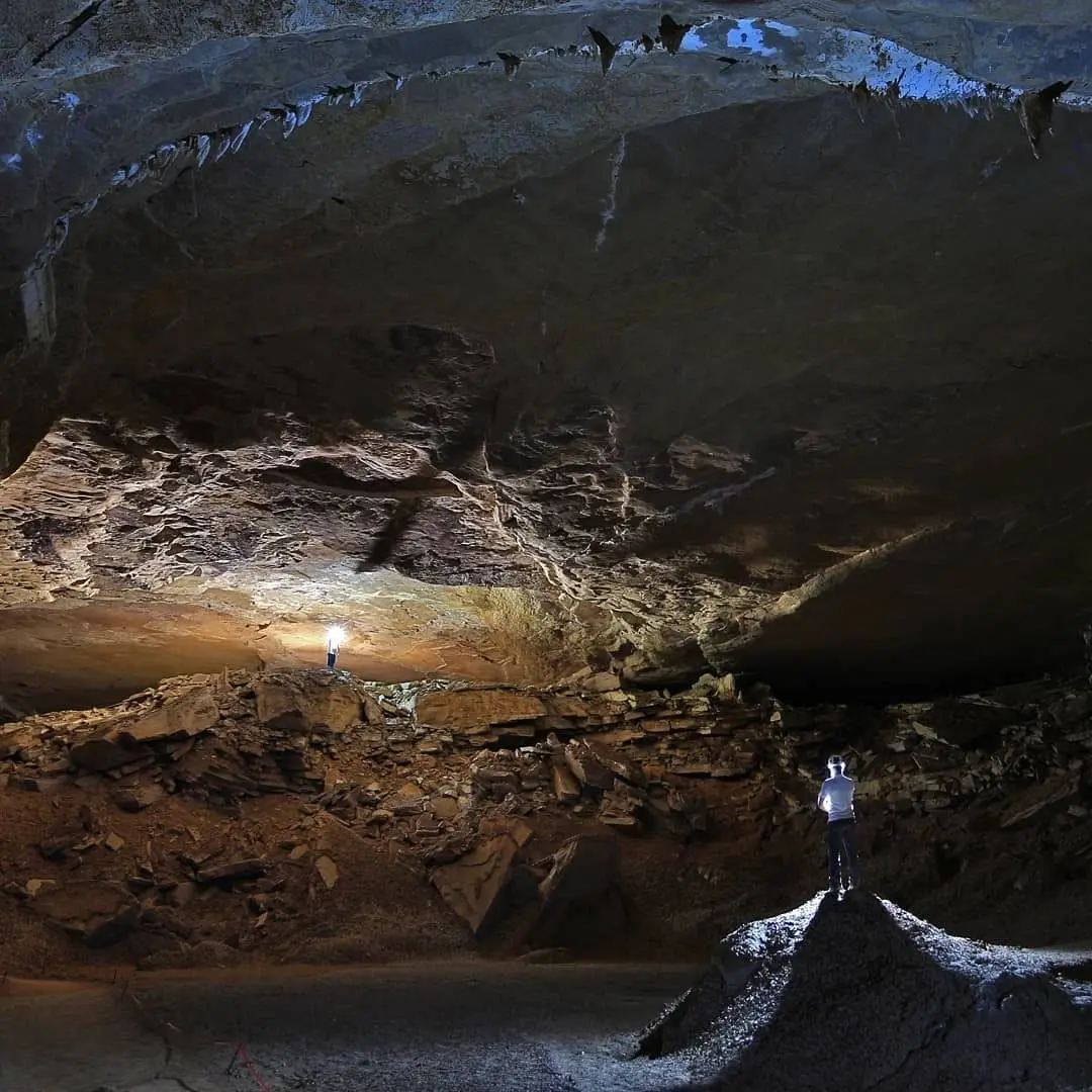 Huge cave chamber lit by the flashlights of two people