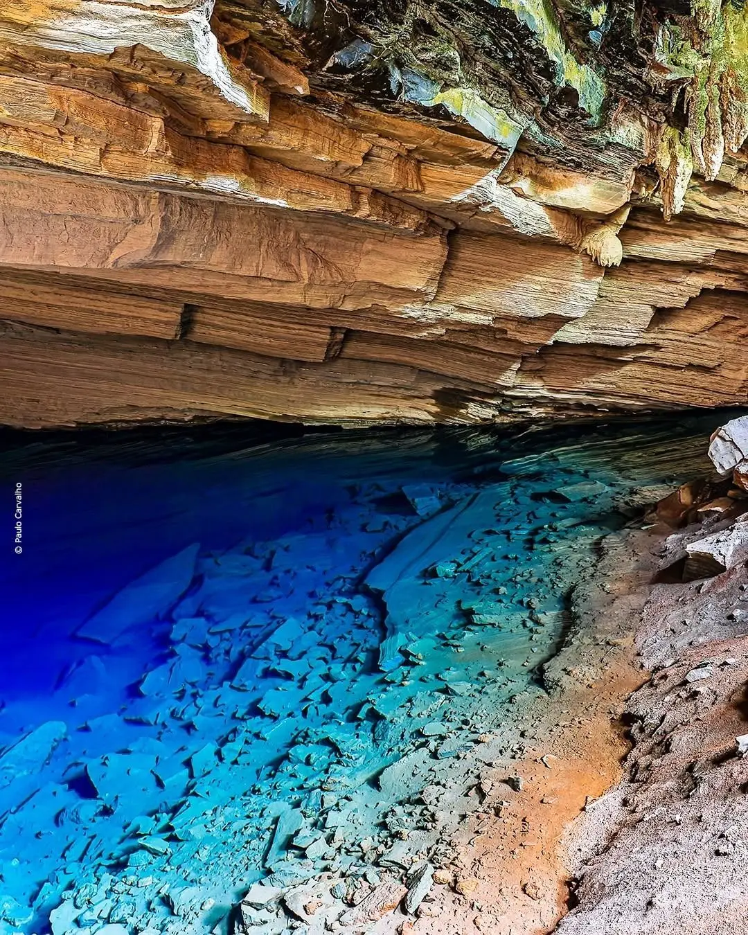 Deep blue water under the low, layered rock ceiling of the Gruta Azul, with stone slabs visible on the bottom