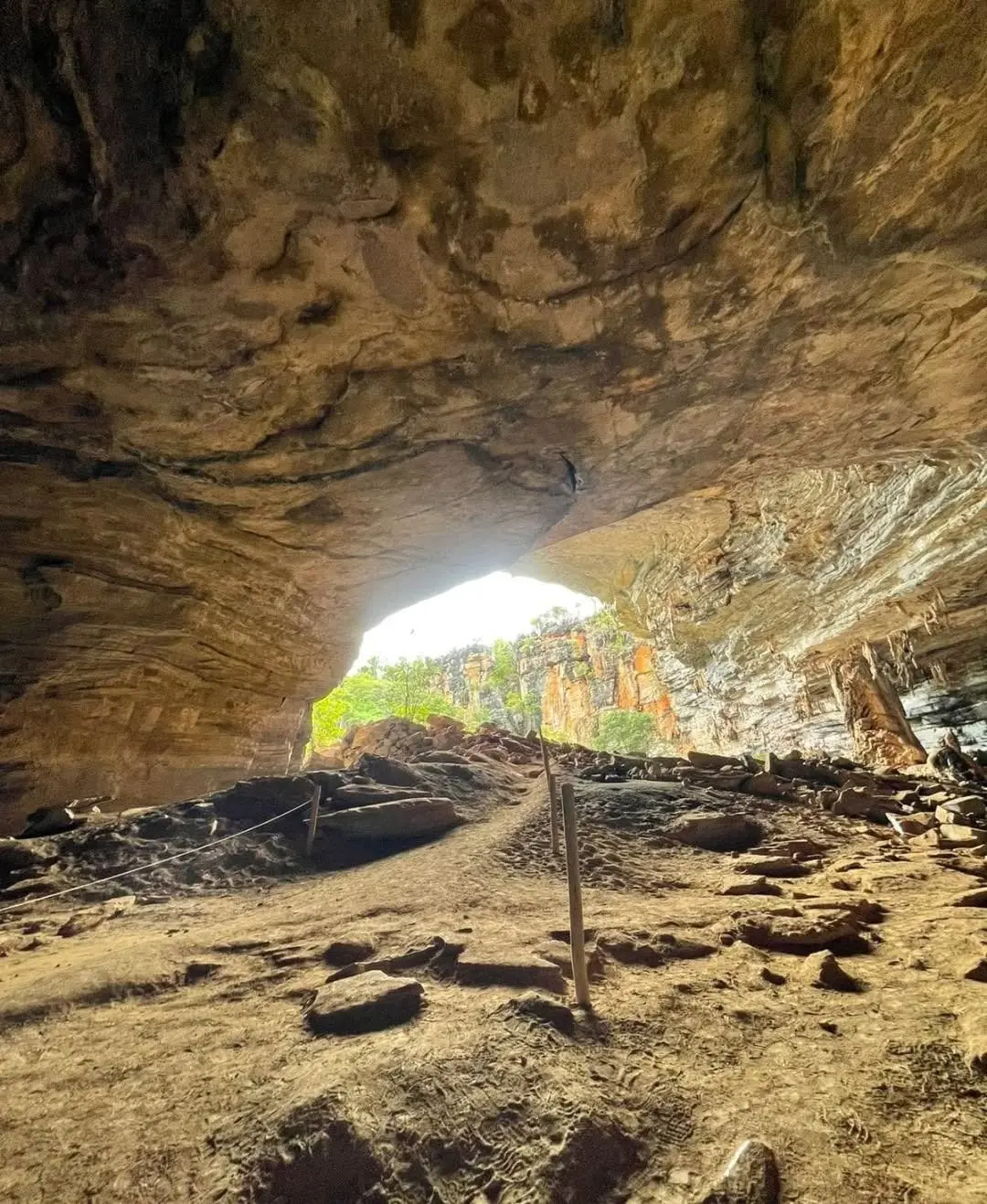 Entrance chamber of the Gruta da Lapa Doce: dirt floor, a path marked with rope and the opening to the forest beyond