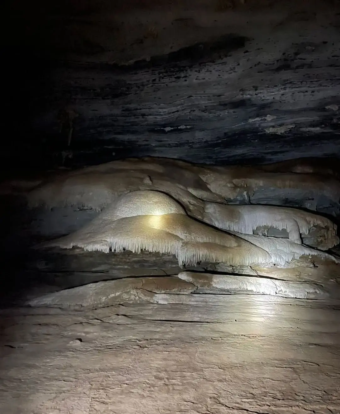 Pale limestone formations lit by a flashlight in the dark chamber of the Gruta da Lapa Doce