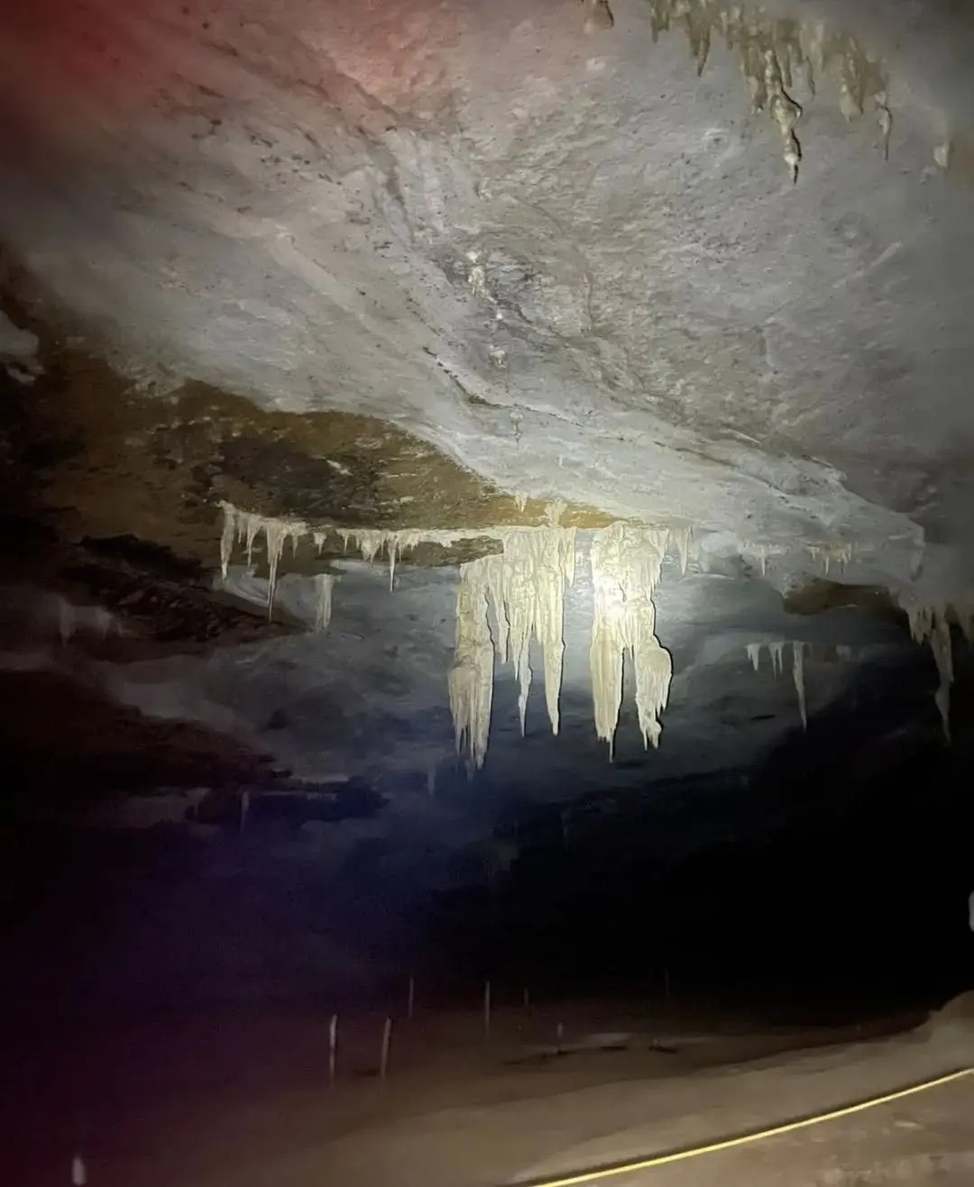 White stalactites hanging from the dark ceiling of the Gruta da Lapa Doce, lit by a flashlight