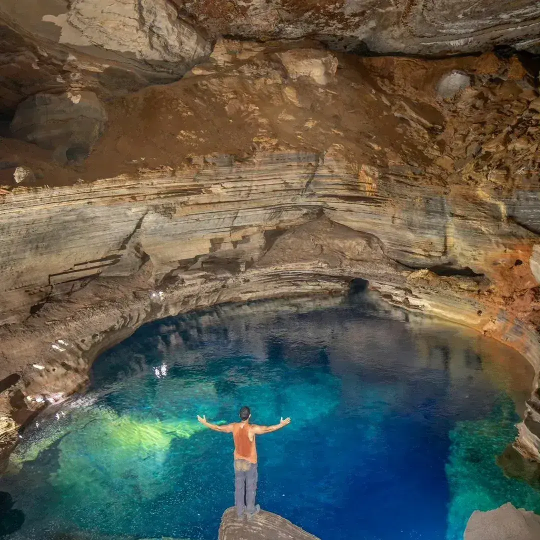 Person with open arms in front of a blue lake inside a cave