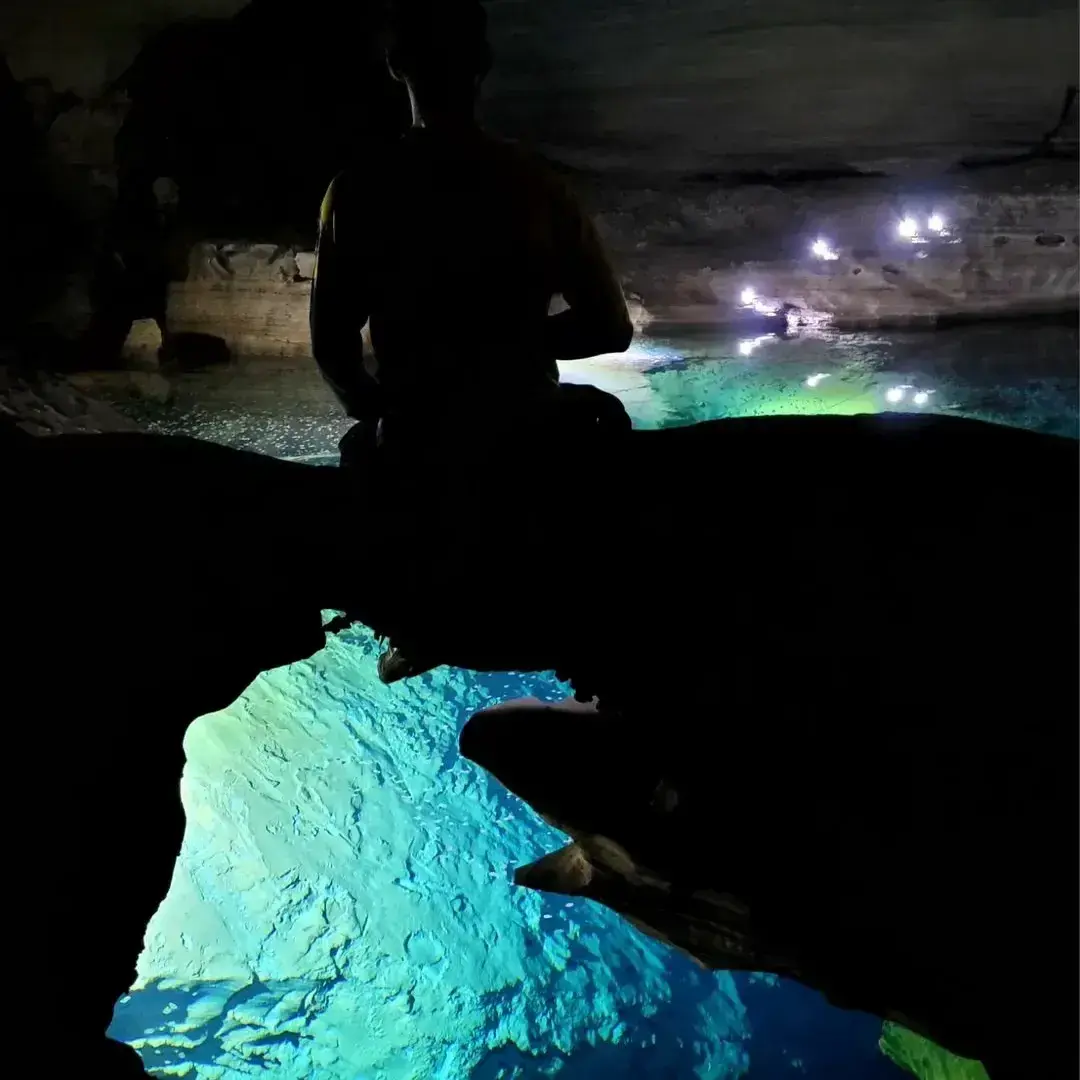Silhouette of a person in front of the blue water deep inside a cave