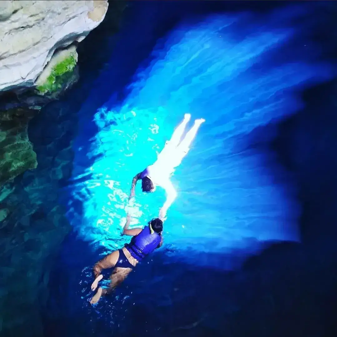 Two people in life vests floating in the beam of blue light at Poço Azul