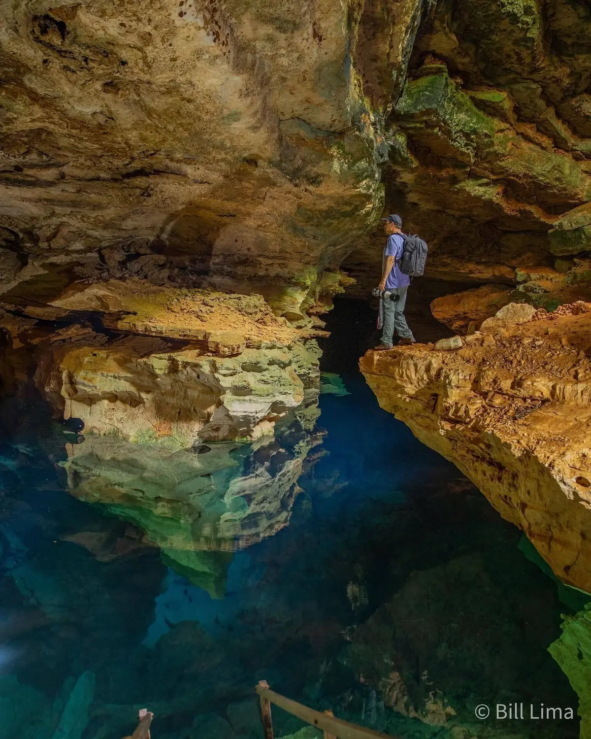 Photographer with a camera on a rock above the glowing blue water of Poço Azul, inside the cave