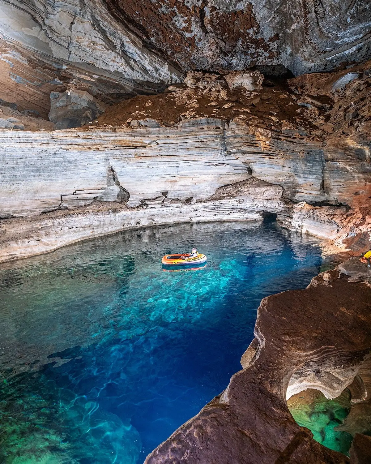 Person on a float on the clear blue water of the Poço do Lima, surrounded by layered rock walls
