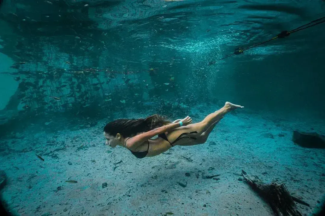 Woman swimming underwater among fish in the Pratinha River, next to the snorkeling guide rope