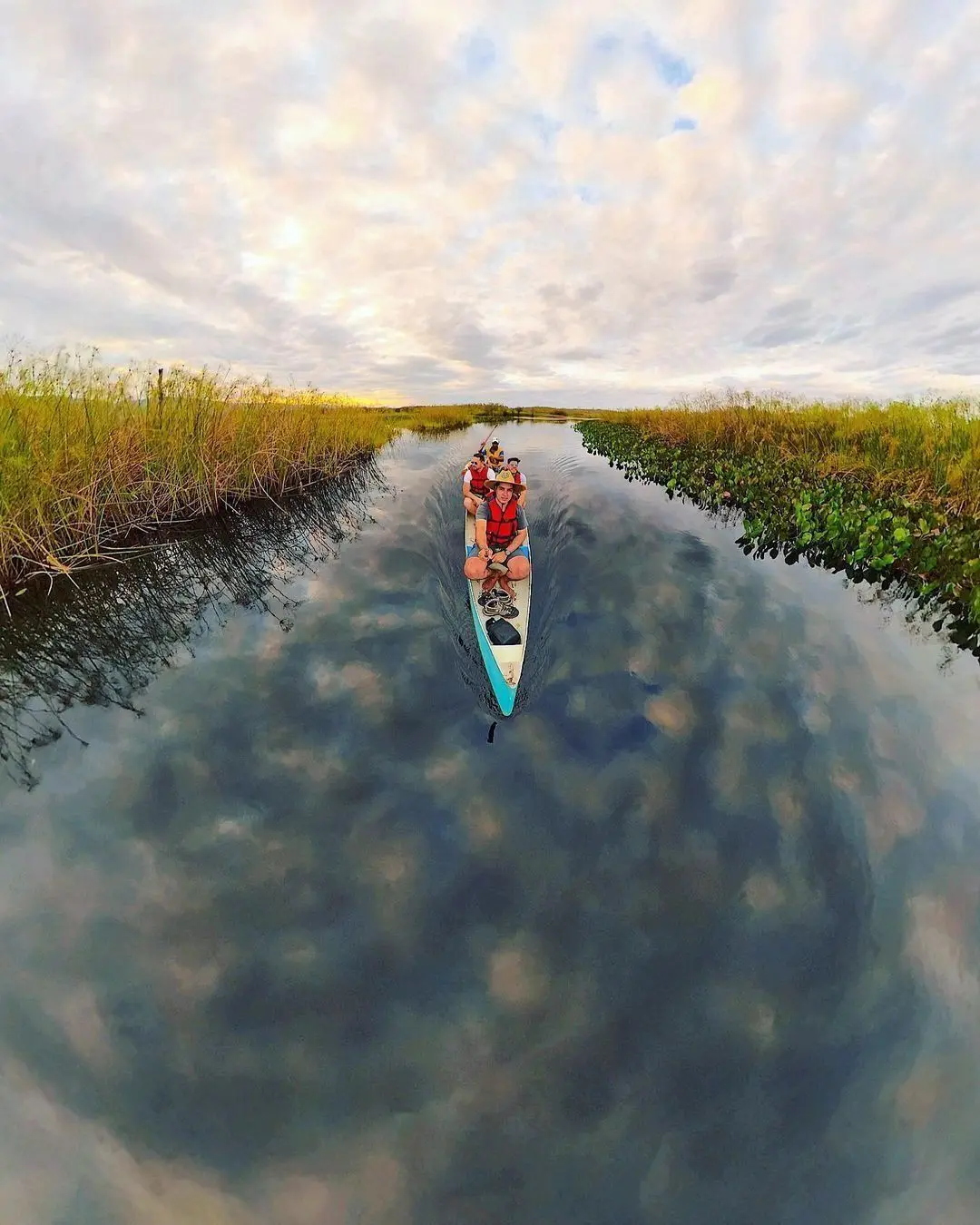 Canoe with four people on a dark-water channel reflecting the clouds