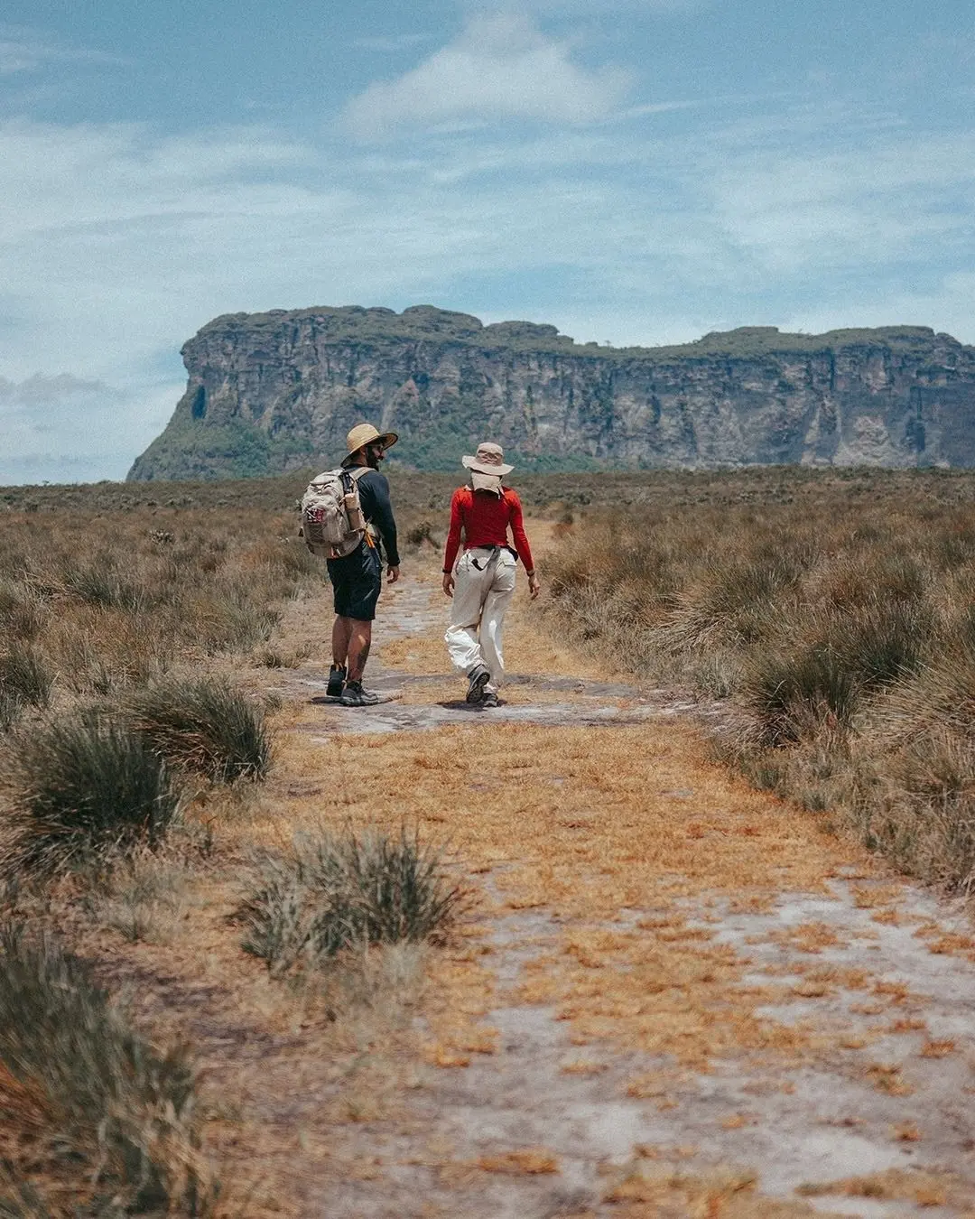 Couple walking on a trail through the gerais, with the Morrão cliff in the background