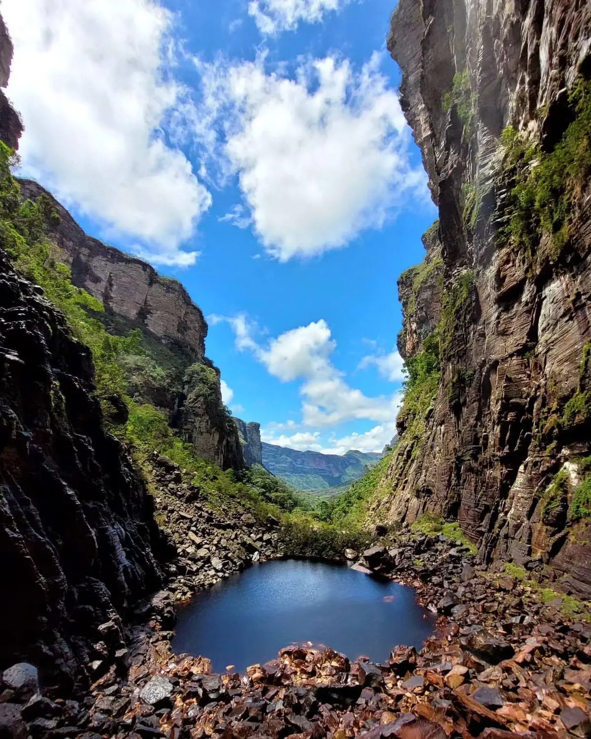 Dark pool at the bottom of a canyon with tall walls, with the valley and blue sky in the background