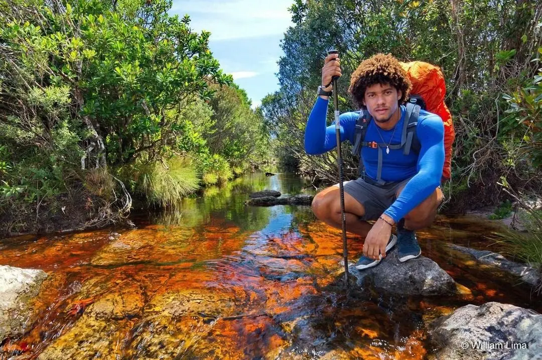 Hiker with a large backpack crouching in a tea-colored stream among shrubs