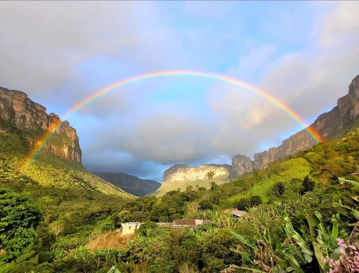 Rainbow over local residents' houses and green cliffs in the Vale do Pati
