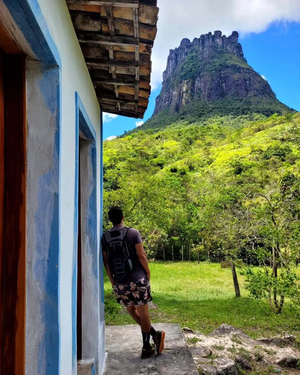 Hiker leaning against a white and blue house, with Morro do Castelo in the background