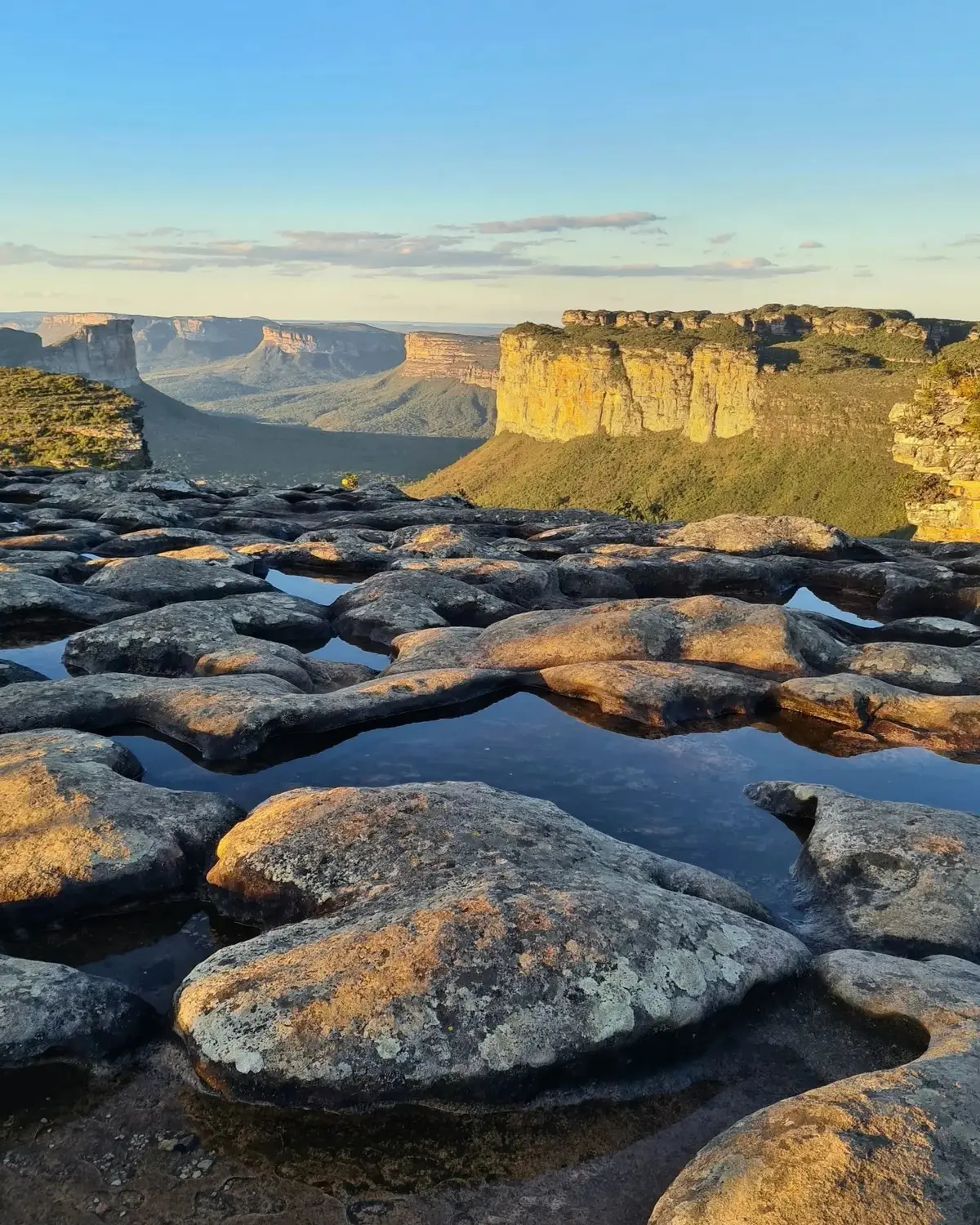 Topo do Morro do Pai Inácio ao pôr do sol: poças de água no lajedo e morros de topo plano iluminados ao fundo