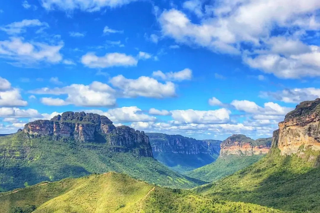 El Vale do Pati visto desde lo alto: cerros verdes cortados por un sendero de tierra, con paredes de cima plana al fondo bajo el cielo azul