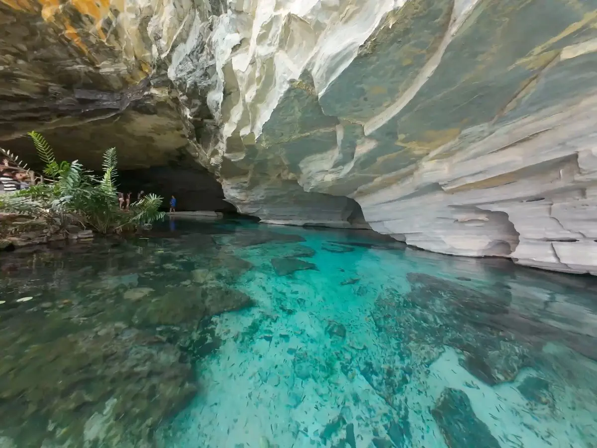 Gruta da Pratinha: agua turquesa transparente bajo una pared de roca clara, con visitantes en la entrada de la gruta