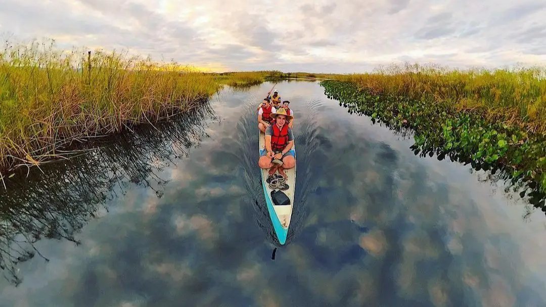 Canoa con cuatro personas en un canal de agua oscura que refleja las nubes