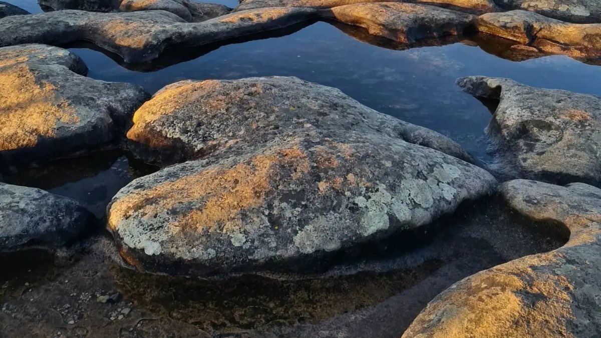 Poças de água no lajedo do topo do Pai Inácio e morros de topo plano iluminados pelo pôr do sol
